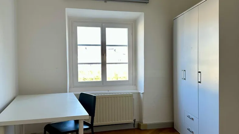 Helles Schlafzimmer mit Parkettboden, weißem Kleiderschrank und Schreibtisch am Fenster.