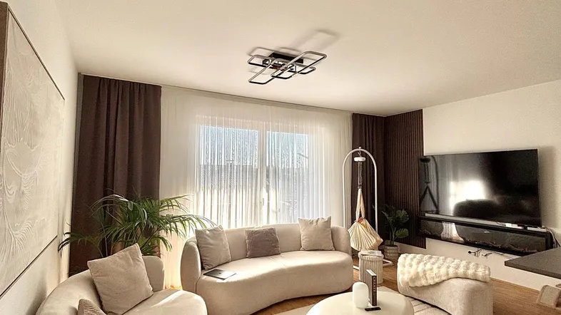Helles Wohnzimmer mit modernen, geschwungenen Sofas, Holzboden und großem Fernseher.