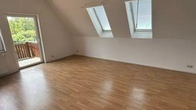 Heller Raum im Dachgeschoss mit Laminatboden, Dachfenstern und Zugang zu einem kleinen Balkon.
