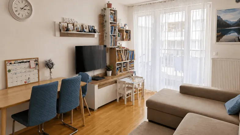 Helles Wohnzimmer mit Holzboden, großem Sofa und Zugang zu einem Balkon.