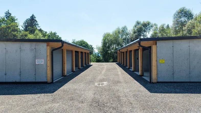 Zwei Reihen moderner Garagen oder Lagereinheiten mit Betonwänden und Holzelementen, umgeben von Natur.