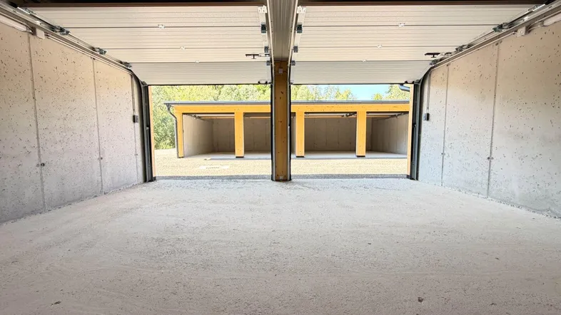 Innenansicht einer modernen Garagenbox mit Betonwänden und Blick auf weitere Carports im Freien.