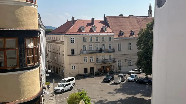 Blick von oben auf eine historische Gasse mit Gebäuden und einem kleinen Außenbereich mit Tischen.