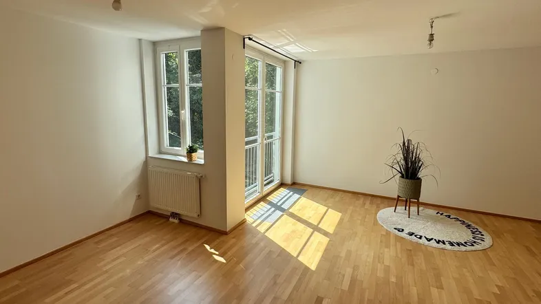 Helles Zimmer mit Parkettboden, weißen Wänden und Zugang zu einem französischen Balkon.