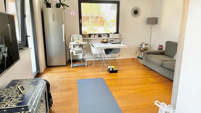 Heller Wohn- und Essbereich mit Holzboden, einem Sofa, Esstisch und Zugang zu einem Balkon.