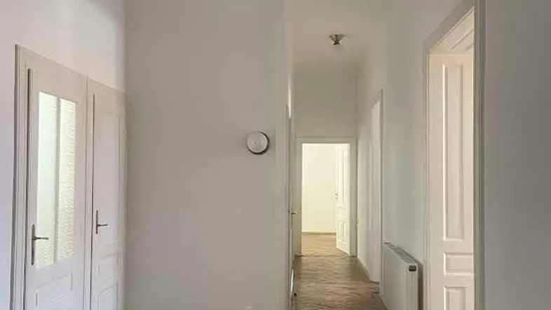 Langer Flur mit Fischgrätparkett, weißen Wänden und einem klassischen Deckenleuchter.