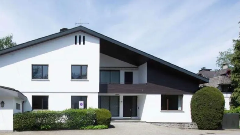 Modernes Haus mit weißer und dunkelbrauner Fassade, schrägem Dach und gepflegter Auffahrt.