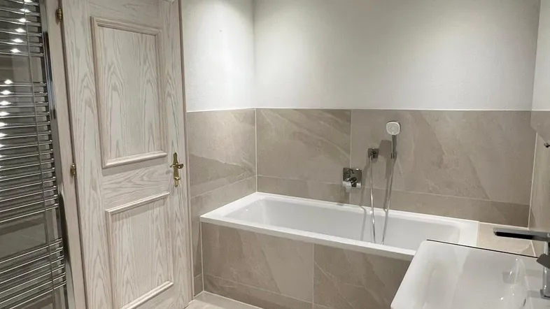 Modernes Badezimmer mit Badewanne, Waschbecken, Fliesenboden und beheiztem Handtuchhalter.