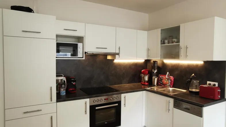 Moderne Küche mit weißen Schränken, dunkler Arbeitsplatte und Holzboden, ausgestattet mit Backofen und Mikrowelle.
