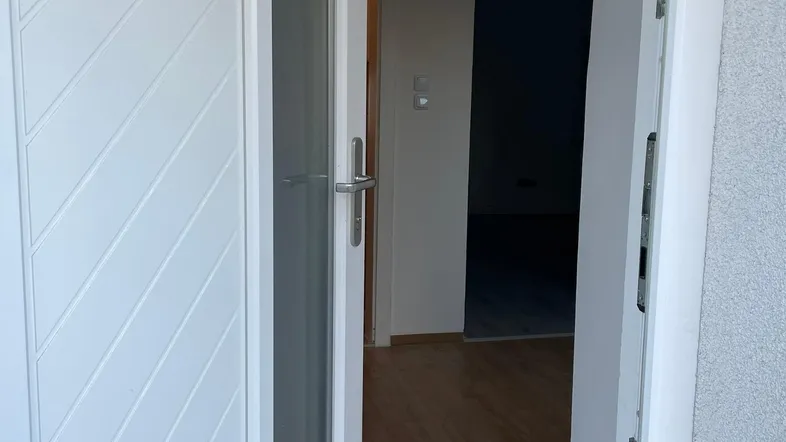 Heller Eingangsbereich mit offener weißer Tür und Laminatboden, der in den Innenraum führt.