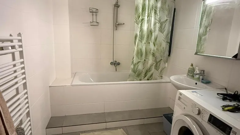 Funktionales Badezimmer mit Badewanne, Duschvorhang, Waschbecken und Waschmaschine.