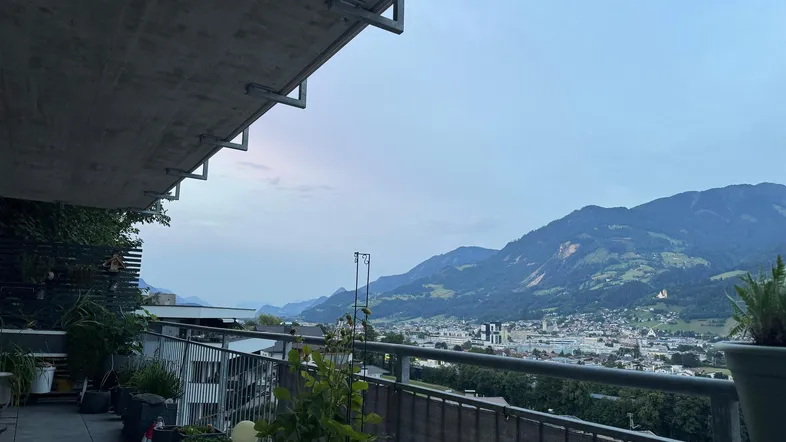 Geräumiger Balkon mit Fliesenboden, Pflanzen und weitem Blick auf die Berge und die Stadt.