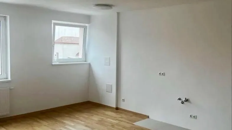 Helles Zimmer mit Parkettboden und weißen Wänden, bereit für die Einrichtung einer Küche oder eines Wohnbereichs.
