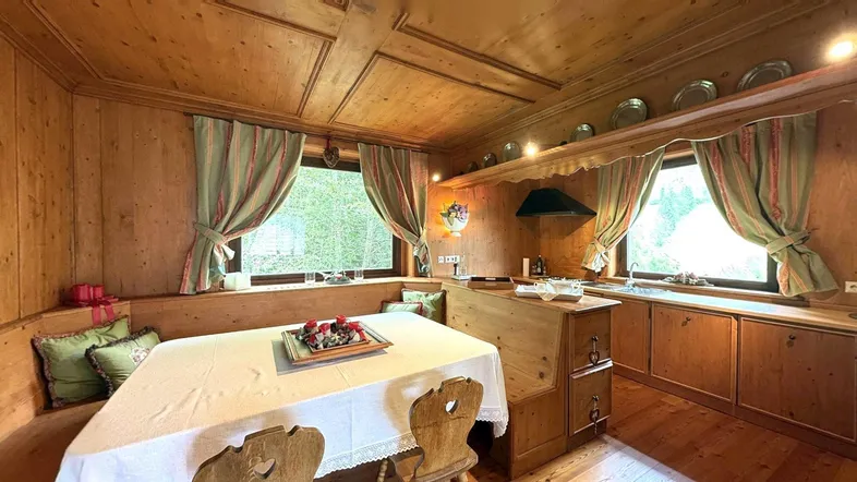Traditionelle Holzküche mit Essbereich, Holztäfelung und Blick ins Grüne durch die Fenster.
