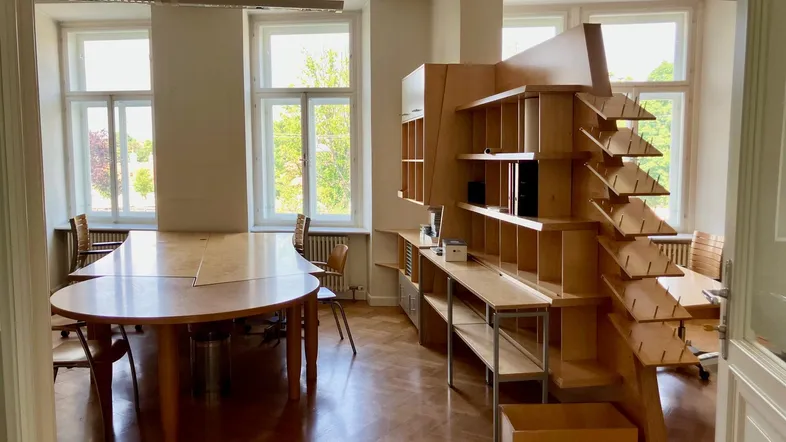 Geräumiges Büro mit großem Konferenztisch, einzigartigem Holzregal und Blick ins Grüne durch hohe Fenster.