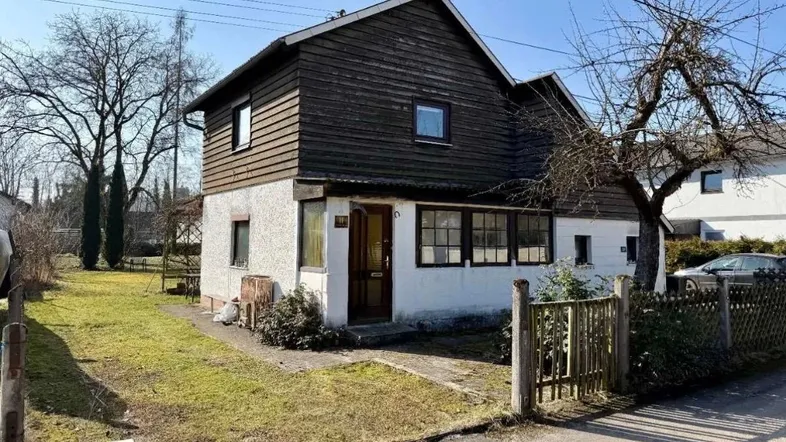 Vorderansicht eines Einfamilienhauses mit weißem Putz, dunkler Holzverkleidung und kleinem Vorgarten.