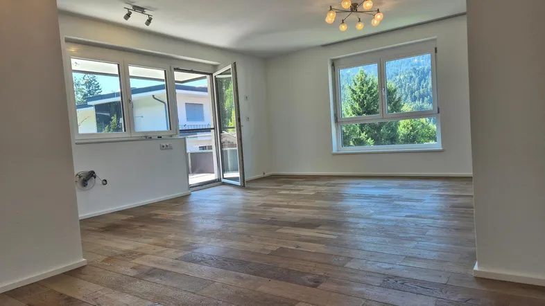 Helles Zimmer mit Holzboden, großen Fenstern und Zugang zu einem Außenbereich mit Bergblick.
