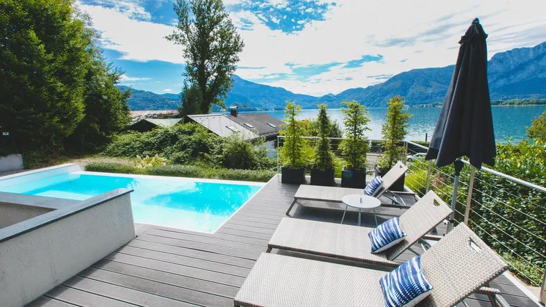 Geräumige Terrasse mit Pool und bequemen Liegestühlen, die einen atemberaubenden Blick auf den See und die Berge bietet.