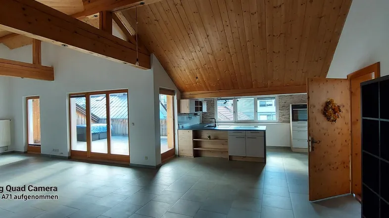 Geräumiger offener Wohnbereich mit Holzbalkendecke, Fliesenboden und Zugang zu einer sonnigen Terrasse.