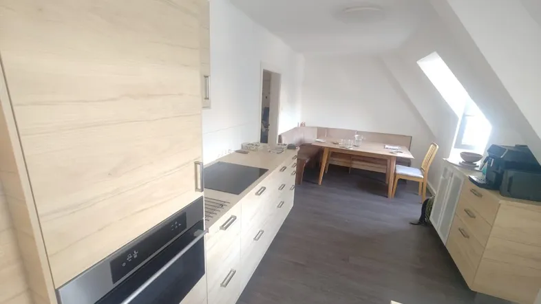 Moderne Küche mit hellen Holzfronten, integriertem Backofen und Essbereich unter Dachschrägen.