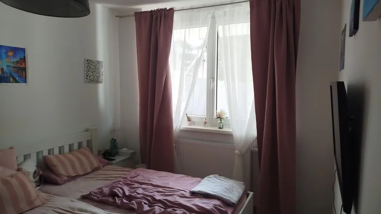 Gemütliches Schlafzimmer mit Doppelbett, Fenster und rosafarbenen Vorhängen für eine entspannte Atmosphäre.