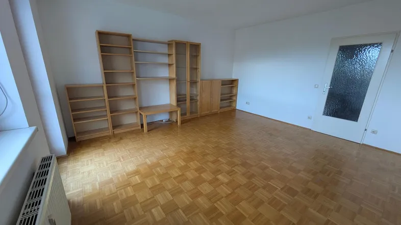 Helles Wohnzimmer mit Parkettboden und Holzregalen, bereit zur individuellen Gestaltung.