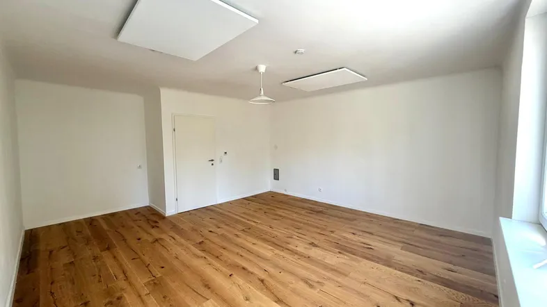 Helles Zimmer mit Holzboden und weißen Wänden, ausgestattet mit Infrarotheizung an der Decke.