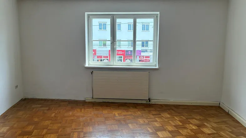 Heller Raum mit Fischgrätparkettboden, weißen Wänden und Blick auf die Straße.
