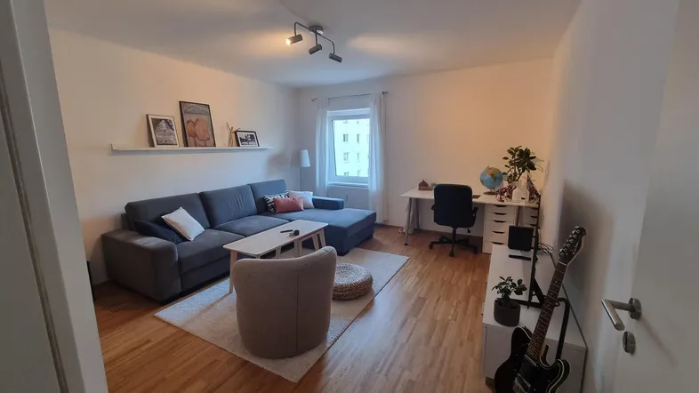 Gemütliches Wohnzimmer mit Sofa, Schreibtischbereich und hellem Holzfußboden.