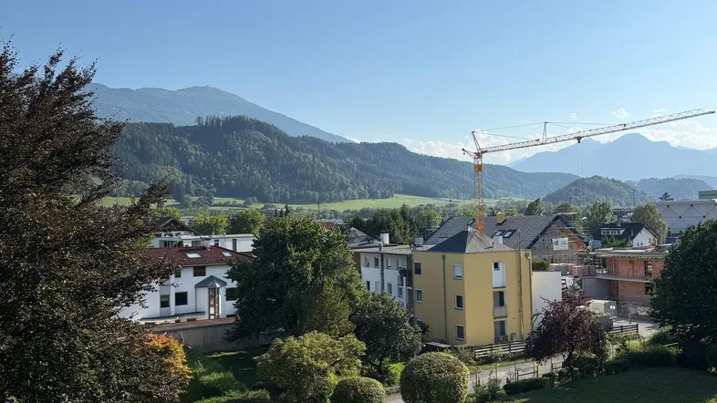 Weitläufiger Blick vom Balkon auf die umliegende Wohngegend mit grünen Hügeln und Bergen im Hintergrund.