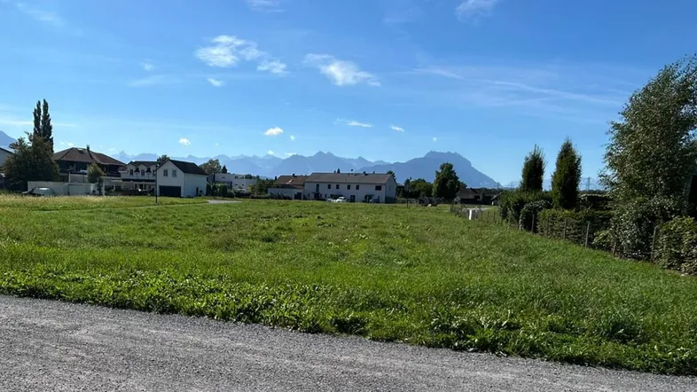 Weitläufiges Grundstück mit grüner Wiese und Bergblick unter blauem Himmel.