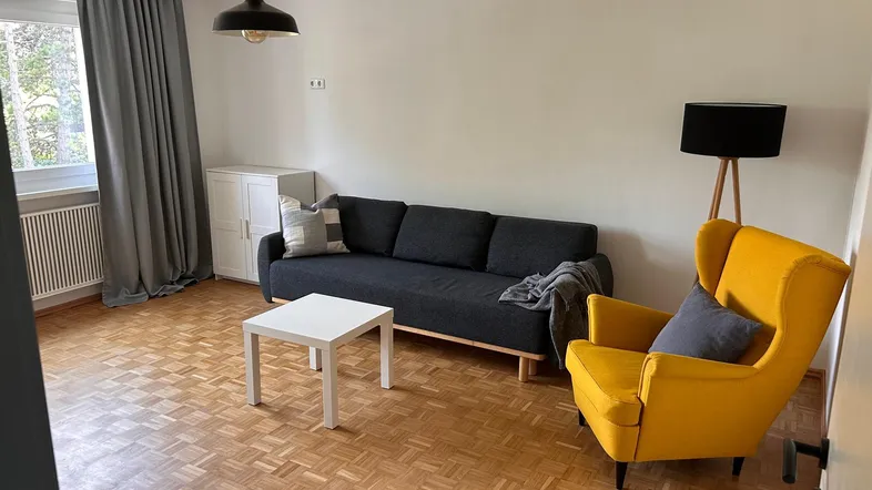 Helles Wohnzimmer mit Parkettboden, bequemer Couch und einem gelben Sessel.