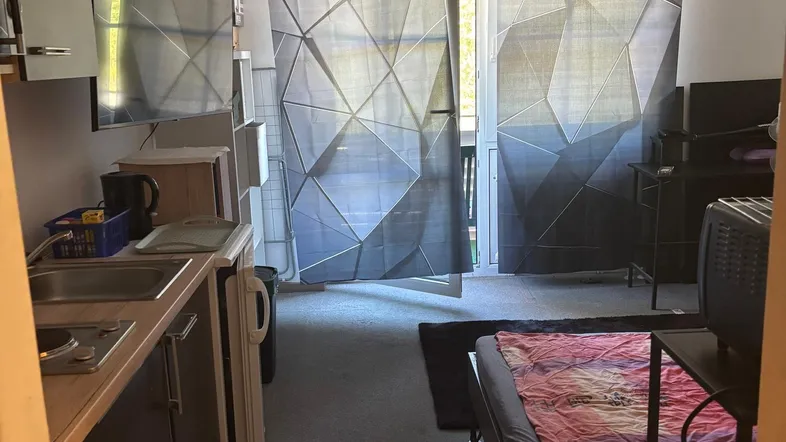 Kompakter Wohnraum mit integrierter Küchenzeile, Schlafbereich und Zugang zum Balkon.