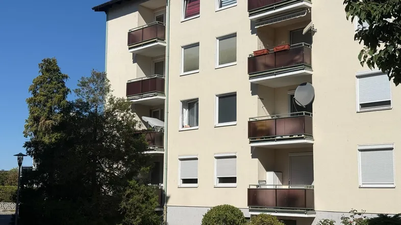 Außenansicht eines Mehrfamilienhauses mit mehreren Balkonen unter blauem Himmel.
