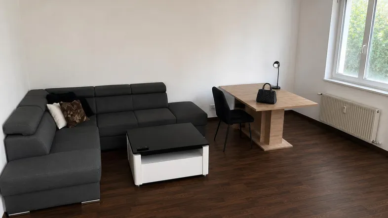 Heller Wohn- und Essbereich mit modernem Sofa, Esstisch und dunklem Laminatboden.