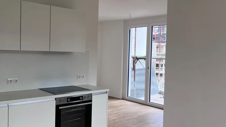 Moderne Einbauküche mit weißen Schränken und Holzboden, angrenzend an einen hellen Wohnbereich mit Balkonzugang.
