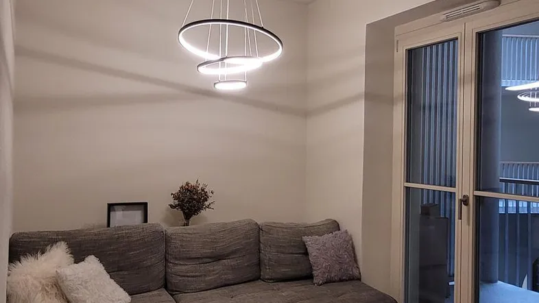 Modernes Wohnzimmer mit Ecksofa, Holzboden und Zugang zum Balkon.