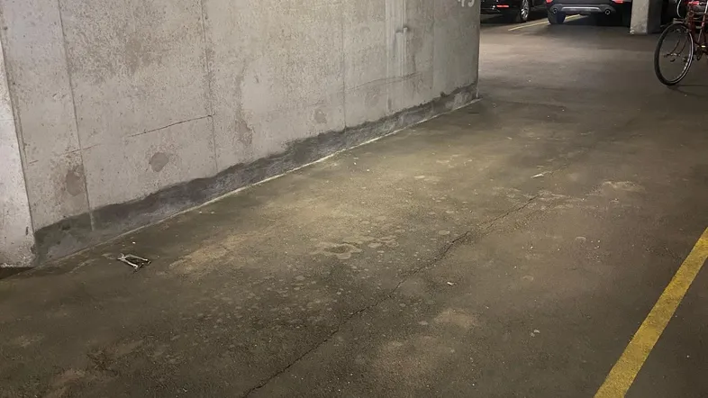 Tiefgarage mit Betonwänden, Asphaltboden und Leuchtstoffröhrenbeleuchtung, bietet Stellplätze für Fahrzeuge.