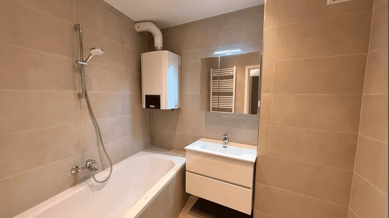 Modernes Badezimmer mit Badewanne, Waschtisch und Wandheizkörper, in hellen Beigetönen gefliest.