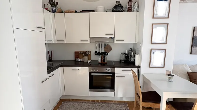Moderne Küche mit weißen Schränken, dunkler Arbeitsplatte und kleinem Essbereich auf Holzfußboden.