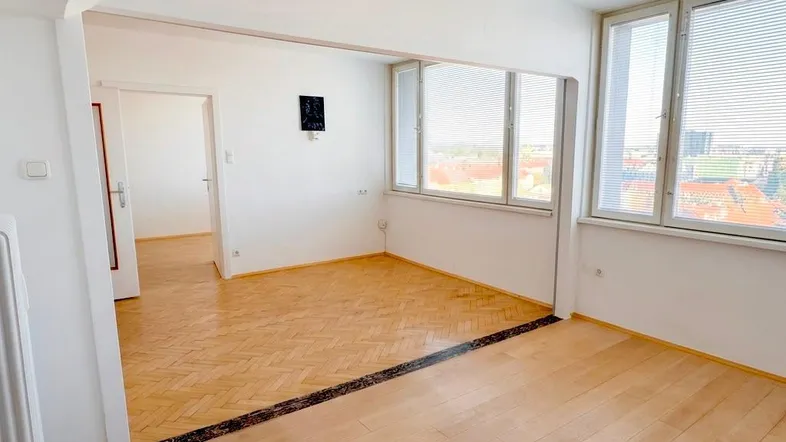 Helles Wohnzimmer mit zwei verschiedenen Parkettböden, großen Fenstern und Heizkörper.