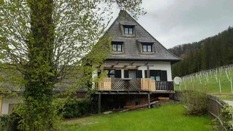 Traditionelles Haus mit spitzem Dach und Balkon in ländlicher Umgebung.