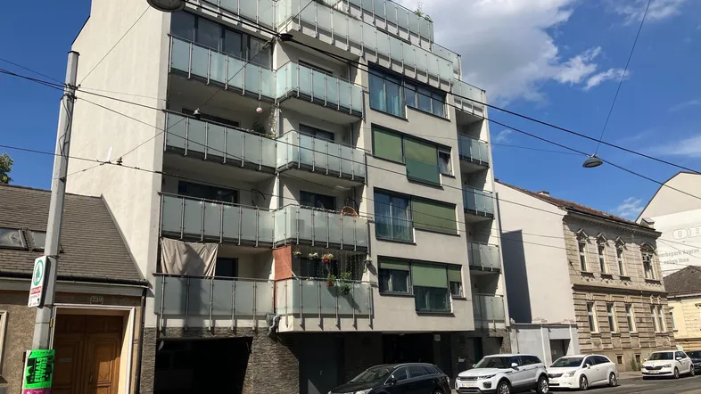 Modernes Mehrfamilienhaus mit Balkonen und Glasbrüstungen an einer belebten Straße.