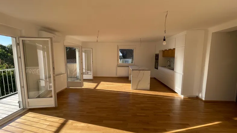 Heller offener Wohn-Essbereich mit moderner Küche, Parkettboden und Zugang zum Balkon.