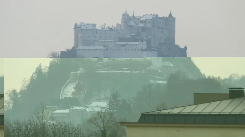 Fernblick auf eine historische Burg auf einem Hügel, umgeben von Bäumen und Nebel.