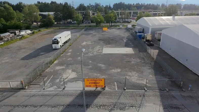 Luftaufnahme eines großen, eingezäunten Industriegrundstücks mit einem Lastwagen und einem 'Zu vermieten'-Schild.