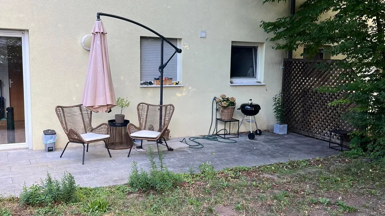 Gemütliche Terrasse mit Gartenmöbeln, Sonnenschirm und Grill, angrenzend an eine kleine Rasenfläche.