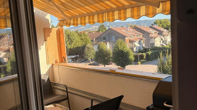 Gemütlicher Balkon mit Markise, Sitzgelegenheiten und Blick auf die umliegende Wohnsiedlung.