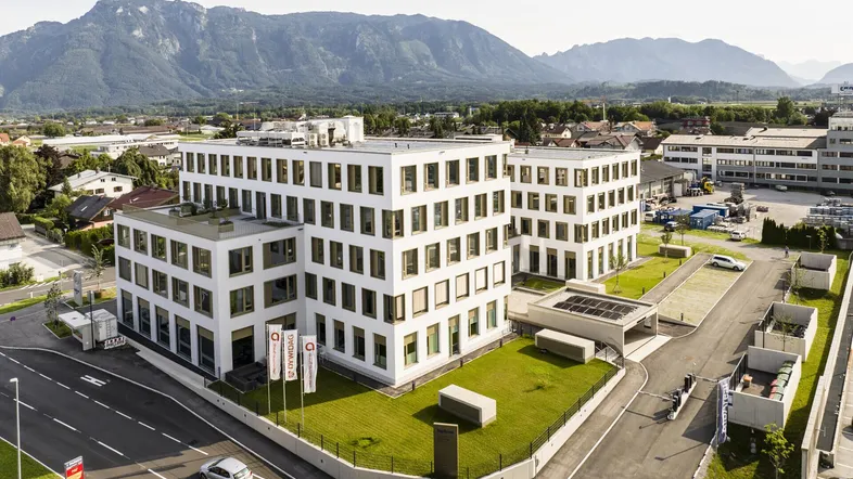 Luftaufnahme eines modernen Bürogebäudes mit gepflegten Grünflächen und beeindruckendem Bergblick.