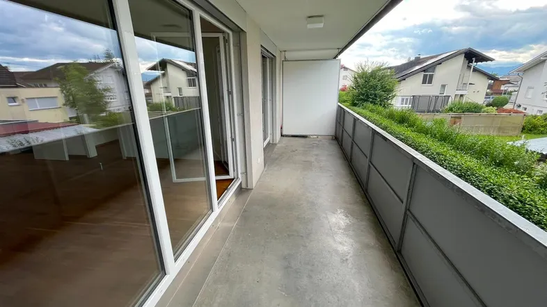 Langer Balkon mit Betonboden und Blick auf die umliegenden Wohnhäuser und grüne Umgebung.
